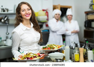 Team of chefs and young beautiful waiter in restaurant kitchen
