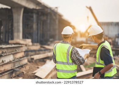 A team of civil engineers and architects wearing safety gear inspect the construction site of a high concrete bridge at a highway construction site. - Powered by Shutterstock