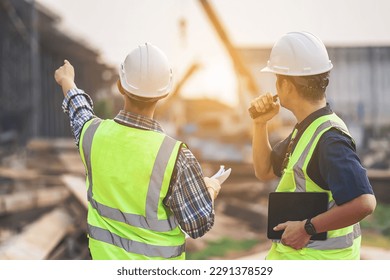 A Team of Civil Engineers and Architects wearing Safety gear Inspect the Construction Site of a High Concrete Bridge at a Highway construction site.