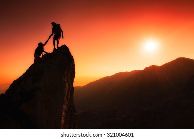 Team Of Climbers Help To Conquer The Summit In Teamwork In A Fantastic Mountain Landscape At Sunset