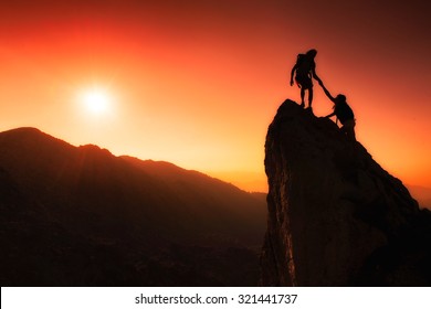 Team Of Climbers Help To Conquer The Summit In Teamwork In A Fantastic Mountain Landscape At Sunset