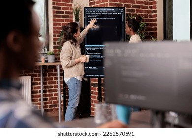 Team of coders talking about algorithms in front of big screen, analyzing html script language. Software developers discussing database on terminal window working in it programming agency