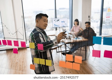 Team collaborating during brainstorming session using sticky notes and charts on glass wall in office. Team members discussing ideas, planning strategy, and analyzing data. - Powered by Shutterstock