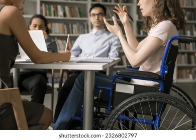 Team of college students and speaker with disability meeting in library, discussing group homework task, class project. Young college girl using wheelchair, talking to classmates. Cropped shot