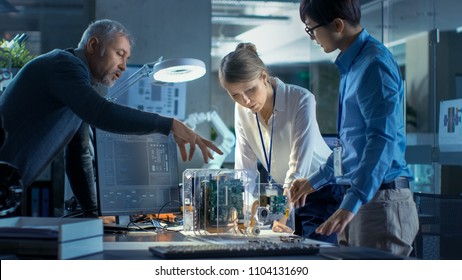 Team of Computer Engineers Lean on the Desk and Choose Printed Circuit Boards to Work with, Computer Shows Programming in Progress. In Background Technologically Advanced Scientific Research Center.