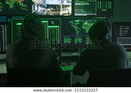 Team of Computer hackers coding on keyboard hidden in illegal hideout full of monitors