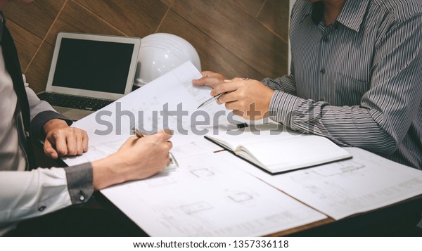 Team of construction engineering or architect\
partner discuss a blueprint while checking information on drawing\
and sketching meeting for architectural project with engineering\
equipment tool.