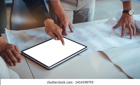 Team of construction engineers discussing paper blueprint and mockup tablet white screen for graphic montage. Architect using technology concept - Powered by Shutterstock