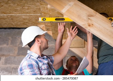 Team Of Construction Workers Building Wooden Staircase, Checking Levels For Accuracy And Quality Control In Unfinished Basement Of New Home