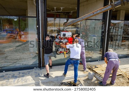 Team of construction workers are installing double glazing using crane and attached glass lifter with system of several vacuum suction cups to hold heavy and large sheet thermo dual pane.