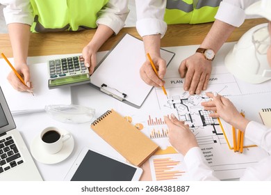 Team of constructors working with house plan at table in room, top view