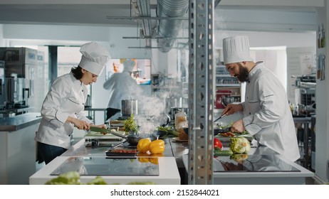 Team Of Cooks Preparing Fresh Ingredients To Follow Culinary Recipe, Making Gastronomic Dish In Authentic Restaurant Kitchen. People Working As Chefs Cooking Gourmet Meal With Vegetables.