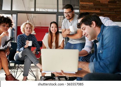 Team Of Creative People Looking At Colleague Showing Project Plan On His Laptop. Diverse Group Of Young People Having A Meeting At The Office. They Are Discussing About New Project.