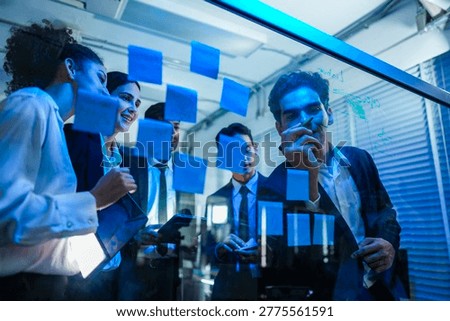Team of cyber security experts collaborating on incident response planning, using a glass board in a modern, blue lit secure office environment.