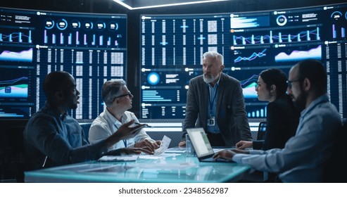 Team Of Data Scientists and Software Developers Discussing Reports in Monitoring Room with Analytics Feed on Big Digital Screen. Senior Man Leading Artificial Intelligence Company Board Meeting - Powered by Shutterstock