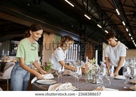 team of decorators organizing festive setting on table with floral decor in celebration hall