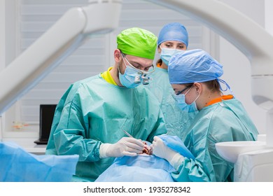 Team of dental surgeons performs surgery on teeth. in a modern clinic. Young dentist. Teamwork. Tooth doctor orthodontist surgeon doing medical operation on root canals. Stomatology office. 