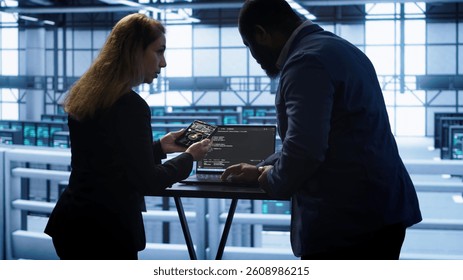 Team of developers doing maintenance checkup using laptop to prolong data center hardware life span. IT support staff members in server hub monitor server infrastructure using notebook, camera A
