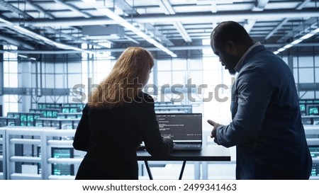Team of developers doing maintenance checkup using laptop to prolong data center hardware life span. IT support staff members in server hub monitor server infrastructure using notebook, camera B