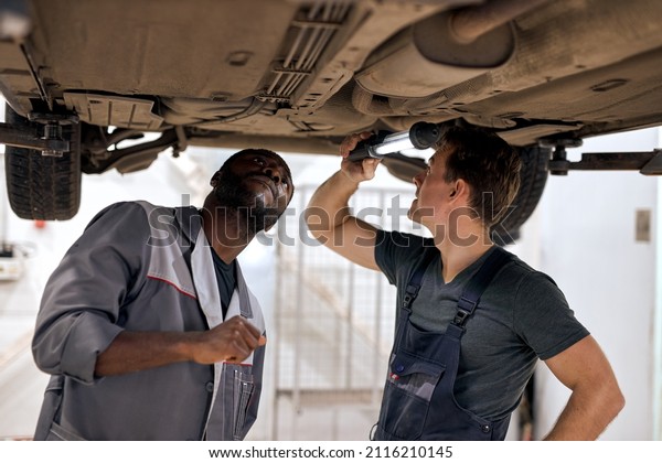 Team of diverse auto mechanics working on\
undercarriage of car diligence attention inspection examination\
annual checkup safety insurance professionalism occupation\
transportation vehicle\
concept