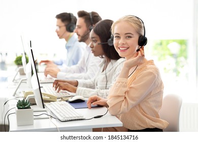 Team of diverse hotline operators with headphones providing service to clients at call center. Young customer support representatives working in telemarketing or telecommunications at modern office