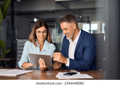 Team of diverse partners mature Latin business man and European business woman discussing project on tablet sitting at table in office. Two colleagues of professional business people working together. - Shutterstock ID 2346448085