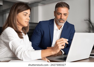 Team of diverse partners mature Latin business man and European business woman discussing project on laptop sitting at table in office. Two colleagues of professional business people working together. - Powered by Shutterstock
