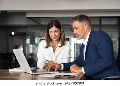 Team of diverse partners sitting at table mature Latin business man and European business woman discussing project on laptop in office. Two colleagues of professional business people working, close up - Powered by Shutterstock