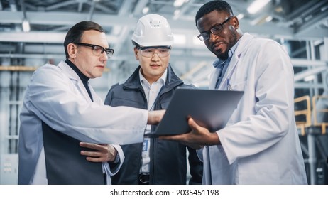 Team Of Diverse Professional Heavy Industry Engineers Wearing Safety Uniform And Hard Hats Working On Laptop Computer. Technician And Workers Talking On A Meeting In A Factory Facility.