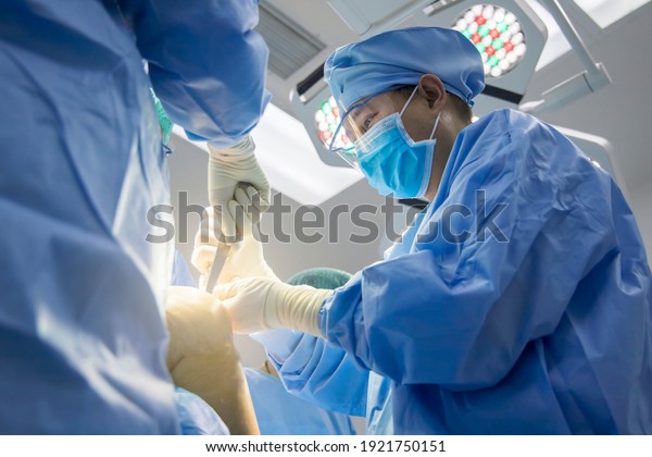 Team of doctor in blue surgical gown suit\
working inside modern operating room.Surgeon perform total knee\
replacement surgery in osteoarthritis patient with protective\
glasses.Medical concept.