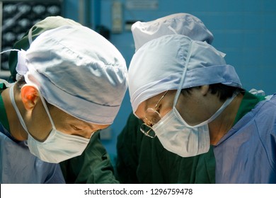 Team Of Doctor Doing General Surgery In Operating Room With Dramatic Light And Dark Background. Surgeon In Blue Surgical Gown Suite And Mask. Medical Concept.