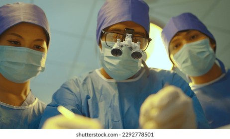 Team doctor with safety glasses and surgical headlight, They is doing surgery with determination inside the operating room, concept of health care. - Powered by Shutterstock