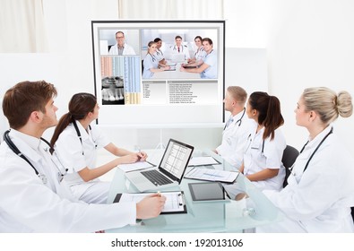 Team of doctors looking at projector screen in video conference meeting at hospital