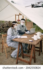 Team Of Doctors In Safety Face Shields Sitting At Table In Tent And Working With Medical Cards Of Refugees At Remote Area