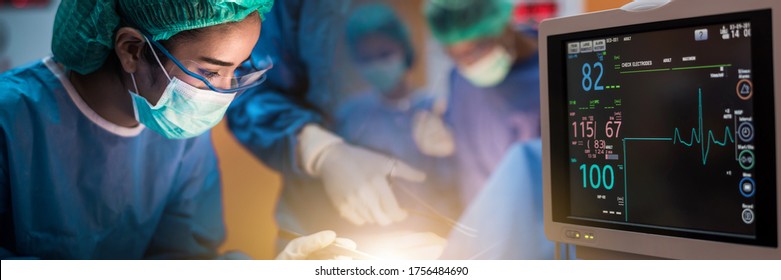 Team Of Doctors Or Surgeons With Electrocardiogram Monitor In Hospital Surgery Operating Emergency Room Showing Patient Heart Rate, During Coronavirus Or Covid-19 Crisis, Medical Concept.