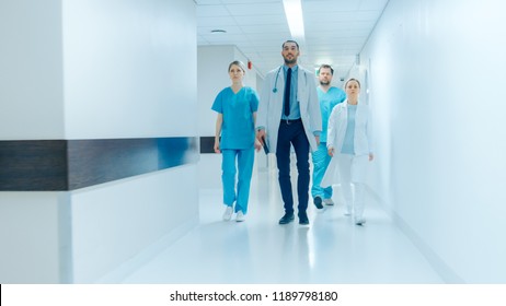 Team Of Doctors, Surgeons And Nurses Walk Through Busy Hospital Hallway, They Talk About Patients, Forthcoming Surgeries And Saving Lives. Clean Modern Hospital With Professional Staff.