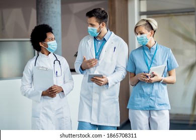 Team Of Doctors Using Touchpad And Communicating While Walking Through A Lobby And Working In The Hospital During Coronavirus Pandemic. 