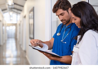 Team Of Doctors Working Together On Patients File At Hospital. Medical Staff Analyzing Report And Working At Clinic. Woman Doctor Having Discussion In A Hospital Hallway With Nurse, Copy Space.