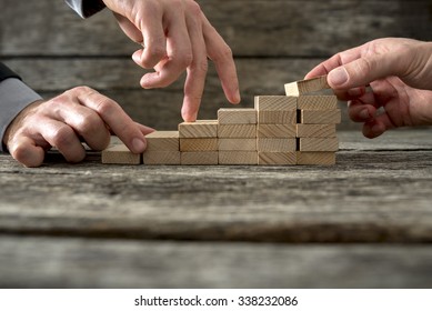 Team effort on the way to success - two male hands building stable steps with wooden pegs for the third one to walk his fingers up towards personal and career growth. - Shutterstock ID 338232086