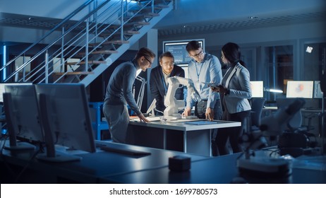 Team Of Electronics Development Engineers Standing At The Desk Working On Robot Arm Prototype. Specialists Working On Ultra Modern Industrial Design, Using Machine Learning, AI And Neural Network