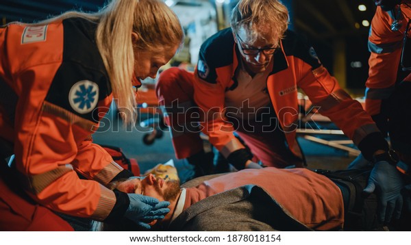 Team of EMS Paramedics Bring a Stretcher from\
Ambulance Vehicle and Help an Injured Young Person. Emergency Care\
Assistants Arrived on the Scene of a Traffic Accident on a Street\
at Night.Blur