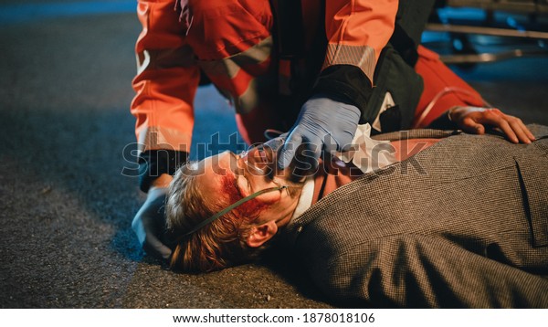 Team of EMS Paramedics Provide Medical Help to an\
Injured Young Man. Doctor in Gloves Attaches Ventilation Mask on a\
Patient. Emergency Care Assistants Arrived in an Ambulance Vehicle\
at Night.