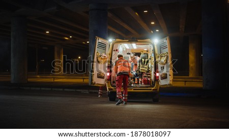 Team of EMS Paramedics React Quick to Provide Medical Help to Injured Patient and Get Him in Ambulance on a Stretcher. Emergency Care Assistants Arrived on the Scene of a Traffic Accident on a Street.