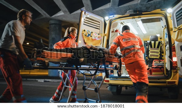 Team of EMS Paramedics React Quick to Provide\
Medical Help to Injured Patient and Get Him in Ambulance on a\
Stretcher. Emergency Care Assistants Arrived on the Scene of a\
Traffic Accident on a Street.\
Blurry