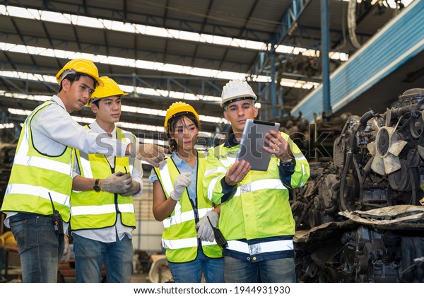 Team of engineers is discussing and viewing\
information from tablets in morning brief before start work The\
head of the engineering team is teaching new engineers at warehouse\
in team work concpet