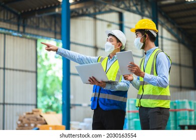 Team Engineers And Foreman Wear A Mask, Hard Hat, And Vest. Standing, Consult Discuss Industrial Production Management Through Data Files With In Mask Factory. Employees Working In The Background.