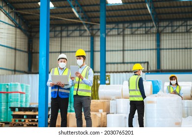 Team Engineers And Foreman Wear A Mask, Hard Hat, And Vest. Standing, Consult Discuss Industrial Production Management Through Data Files With In Mask Factory. Employees Working In The Background.