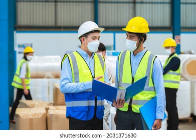 Team Engineers And Foreman Wear A Mask, Hard Hat, And Vest. Standing, Consult Discuss Industrial Production Management Through Data Files With In Mask Factory. Employees Working In The Background.