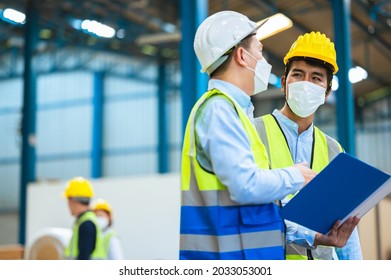 Team Engineers And Foreman Wear A Mask, Hard Hat, And Vest. Standing, Consult Discuss Industrial Production Management Through Data Files With In Mask Factory. Employees Working In The Background.