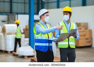 Team Engineers And Foreman Wear A Mask, Hard Hat, And Vest. Standing, Consult Discuss Industrial Production Management Through Data Files With In Mask Factory. Employees Working In The Background.